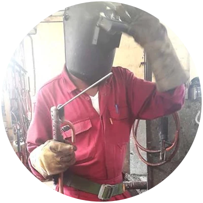 Welder Randy Williams in red overalls and a welding helmet, holding a stick electrode holder.