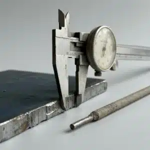 Caliper measuring the thickness of a 1/4 inch steel plate beside a stick rod